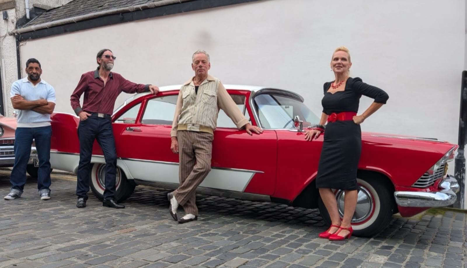The band standing beside a red and white classic car