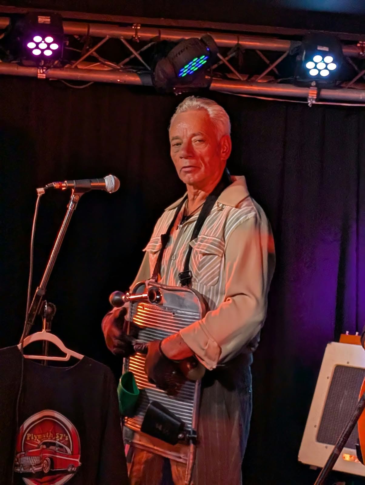 A band member singing and playing guitar in a silver shirt